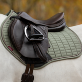 Brown leather saddle on a green quilted saddle pad with a blurred natural background